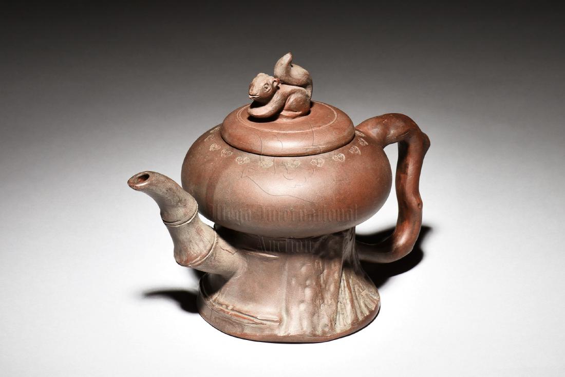 YIXING ZISHA 'SQUIRREL' HIGH STEM TEAPOT: The Yixing Zisha stoneware teapot has compressed body on top of tall stem foot, with bamboo shaped spout and branch shaped handle on the sides, the top mounted with a squirrel shaped finial, the clay 