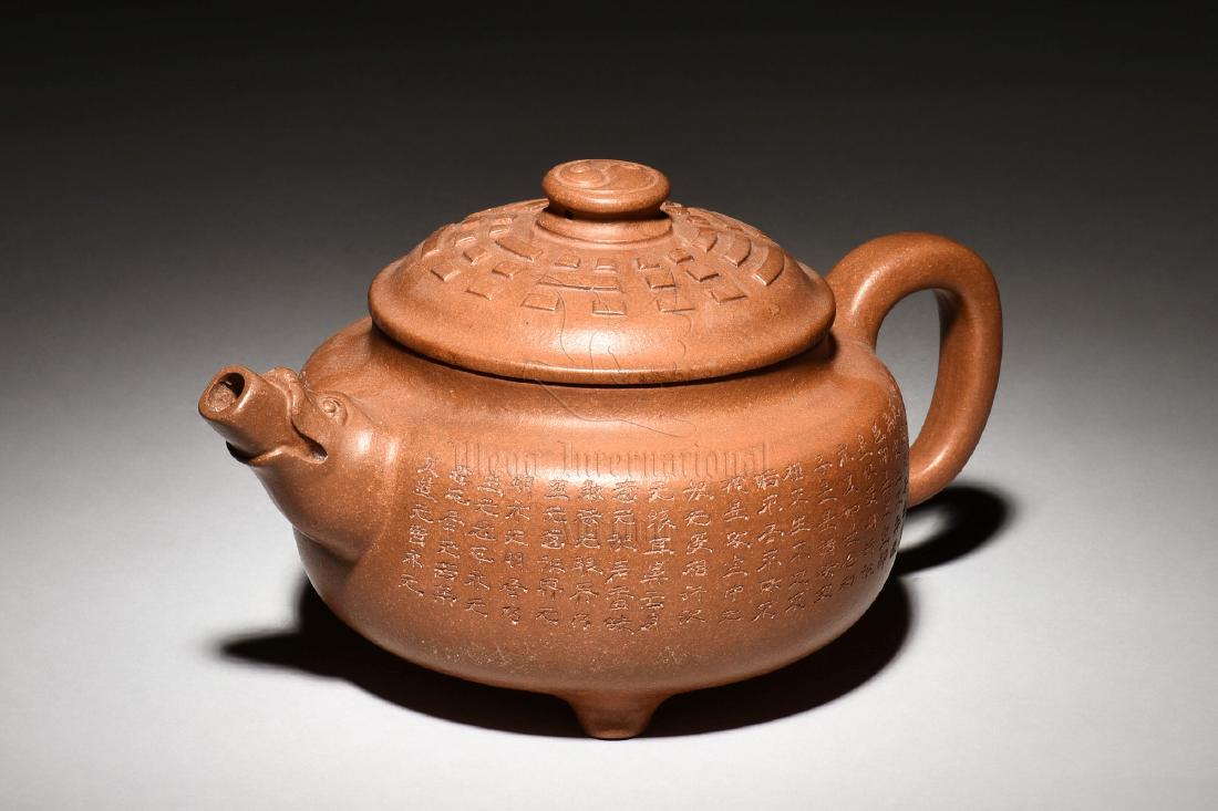 YIXING ZISHA 'POETRY CALLIGRAPHY' TRIPOD TEAPOT: The Yixing Zisha stoneware teapot is of bulbous form, the body inscribed with poetry calligraphy on both sides, stands on three pointed legs, the spout extends from beast mask, and the lid has rectang