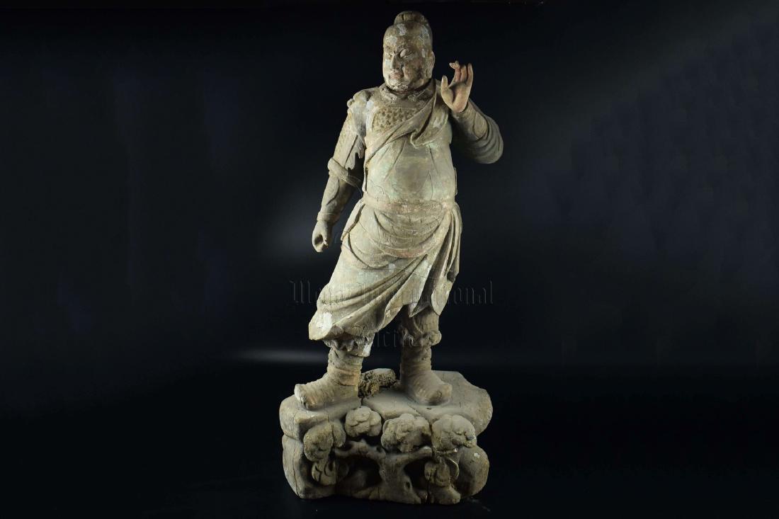 WOOD CARVED 'GUARDIAN' STANDING FIGURE: The wood figure depicts a Guardian standing on a pedestal, wearing full armor with drape, hands raised, eyes open in stern expression, reverse shows hollow interior. Height: 32 3/8 in (82.0 cm) Width: