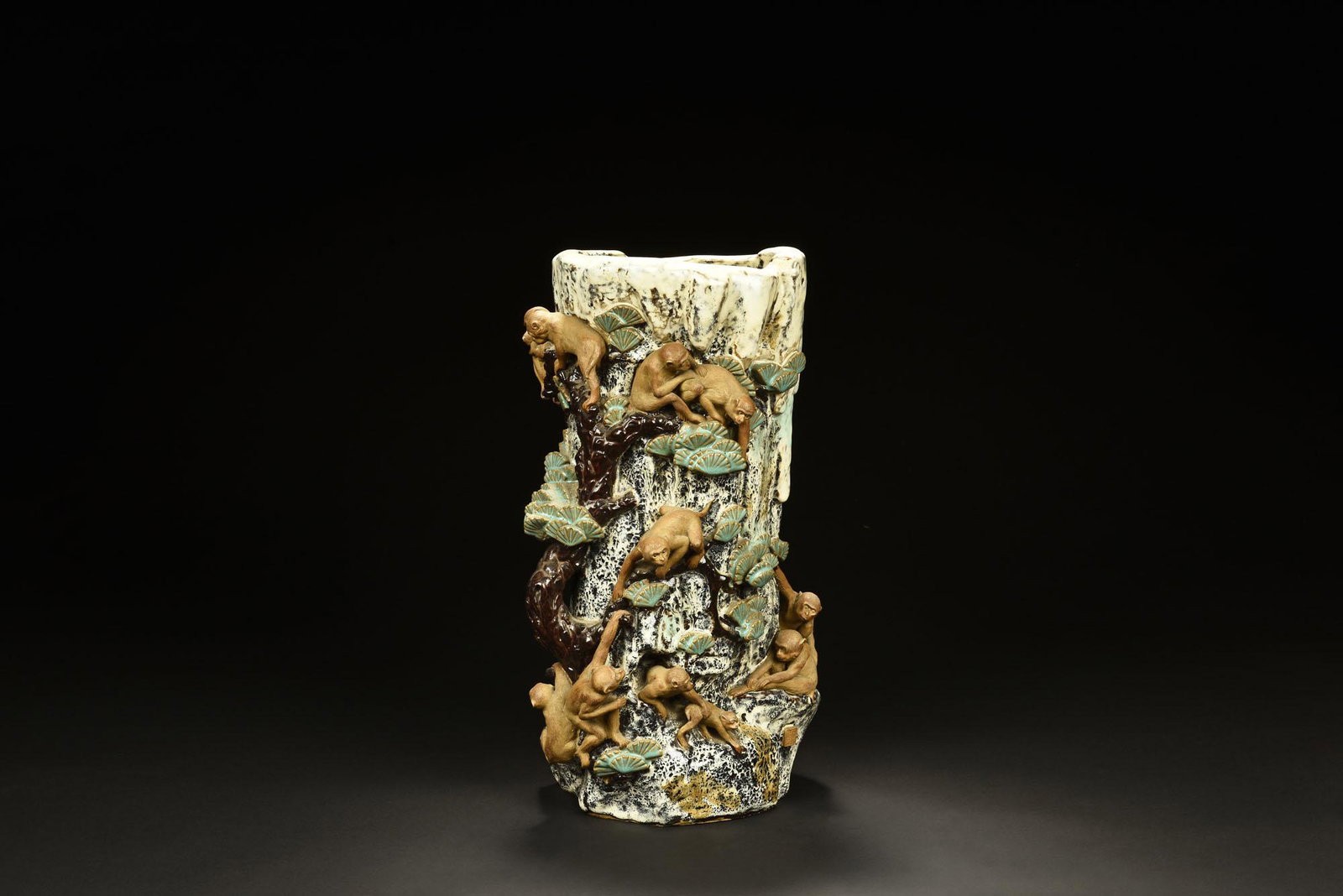 PORCELAIN CARVED 'MONKEYS' BRUSH POT: 瓷雕猴子筆筒 The porcelain carved brush pot depicts a mountain side scene, with monkeys climbing around the cliff and pine trees engaged in various activities, four
