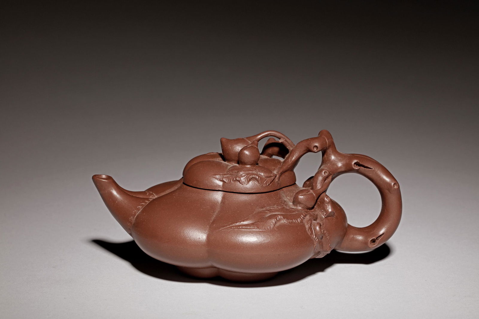 YIXING ZISHA LOBED TEAPOT: 紫砂茶壺 The Yixing Zisha stoneware teapot is of compressed lobed form, the longest dimension measuring Width: 6 1/4 in (15.9 cm), on one side of the body depicts leafy tendril