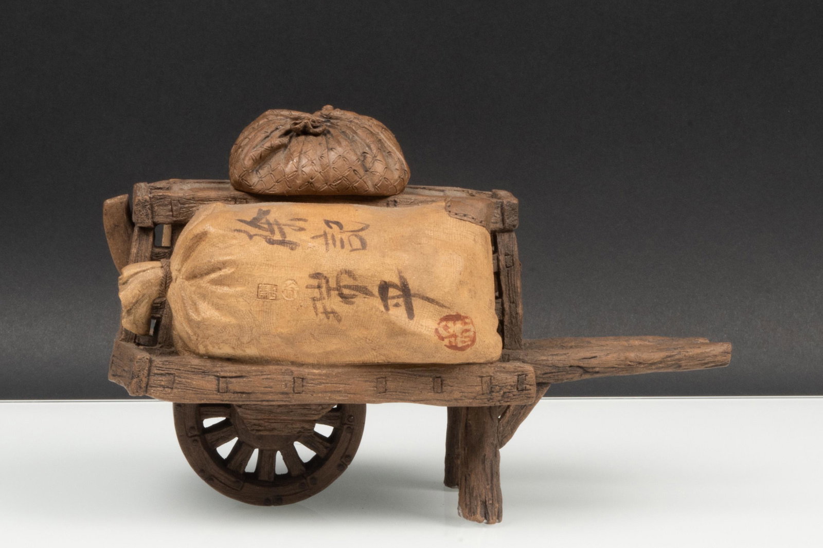ZISHA ‘WHEELBARROW' TEAPOT, 'XU JI RUI PING' MARK: 許記瑞平款 紫砂拉車擺件 Zisha ‘Wheelbarrow' teapot, 'Xu Ji Rui Ping' mark Length:7 in(17.8cm) H:4 3/4 in(12cm)