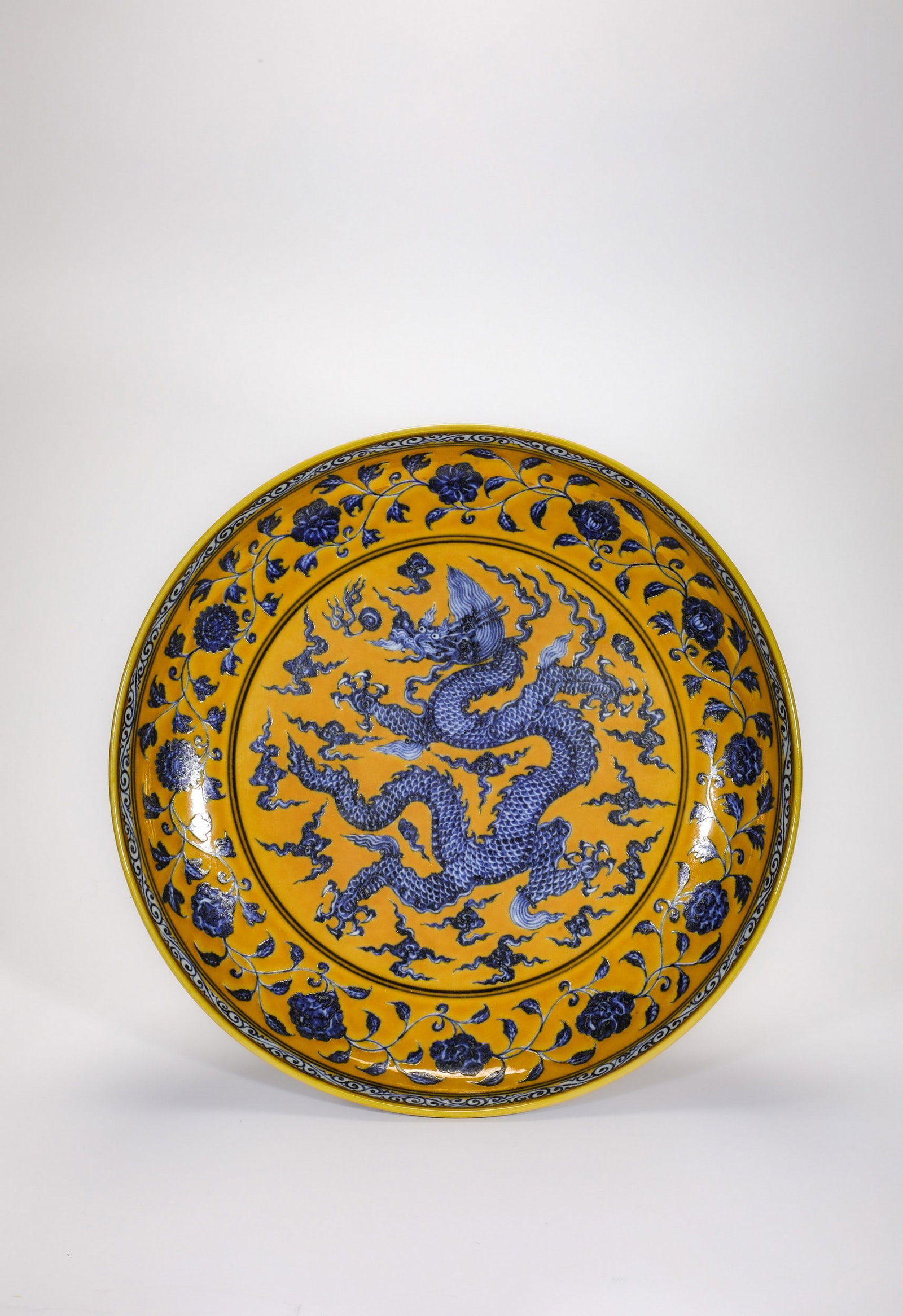 A YELLOW-GROUND BLUE AND WHITE DRAGON DISH: 明宣德黄地青花云龙纹盘 A yellow-ground blue and white dragon dish Diam.34cm Ht.6cm