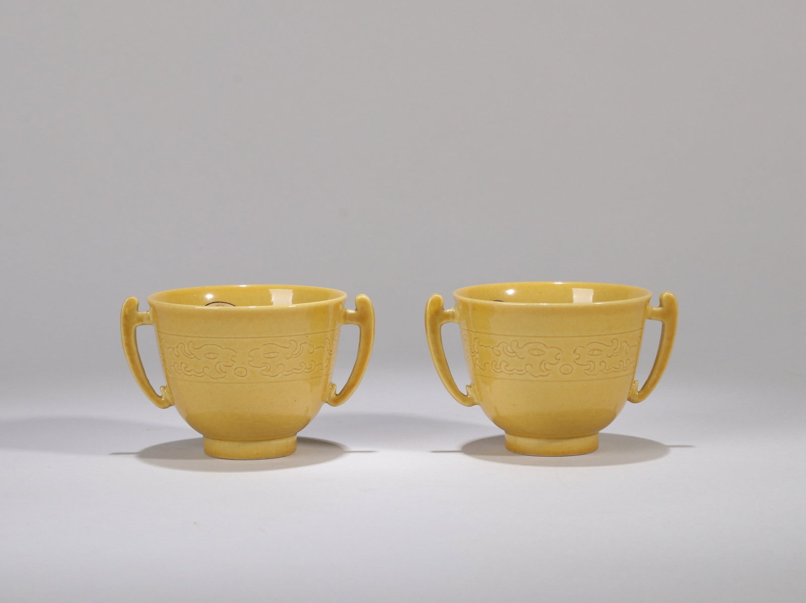 A PAIR OF YELLOW-GLAZED DRAGON CUPS: 清康熙 黄釉暗刻夔龙双耳杯一对 A pair of yellow-glazed dragon cups Ht.4.5cm