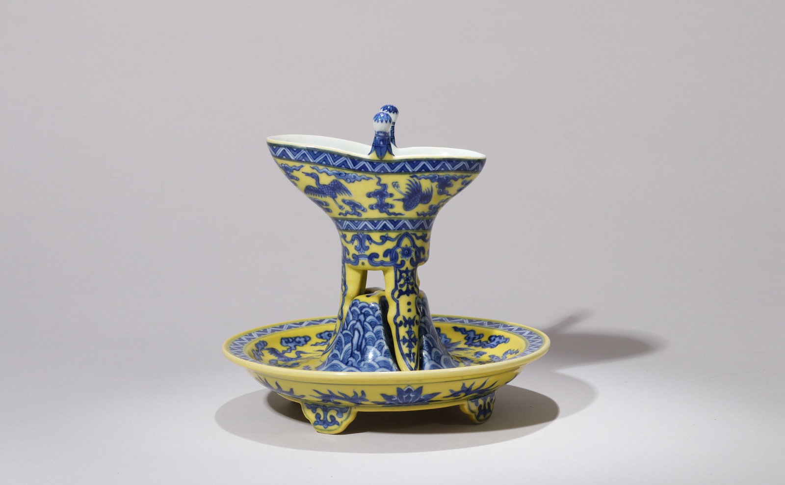 A YELLOW-GROUND BLUE AND WHITE CRANE WINE CUP: 乾隆 黄地青花云鹤纹爵杯 A yellow-ground blue and white crane wine cup Ht.17.5cm Diam.17.5cm