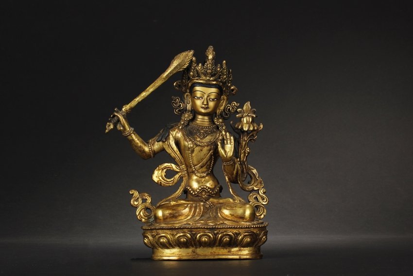 A GILT BRONZE BODHISATTVA FIGURE: Seated dhyanasana on a lotus pad, the Bodhisattva has raised scepter in right hand, vitarka mudra with left hand, wearing flowing robe, beaded ornaments, and decorated crown, eyes open in a calm expre