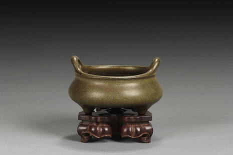 A TEADUST GLAZE TRIPOD CENSER: Of compressed globular form, the censer supported by three short legs, resting on a carved stand, the body in teadust glaze, a pair of uplifting handles on the lipped rim; bottom with four characters