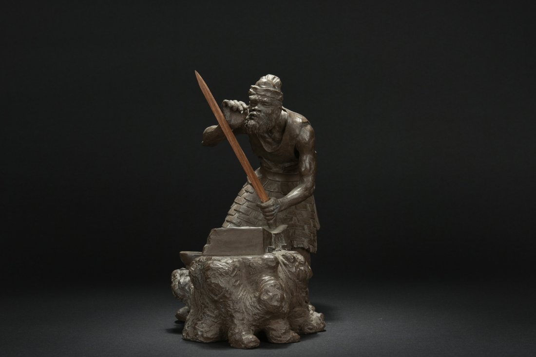 XU XIUTANG: YIXING ZISHA 'SWORDSMITH' SCULPTURE: The Zisha sculpture depicts a sword smith working on the anvil, inspecting the blade of the sword, crafted with fine details, by Master Yixing Maker Xu Xiutang. H: 11 3/4 in (29.8 cm) W: 11 1/2 in (29