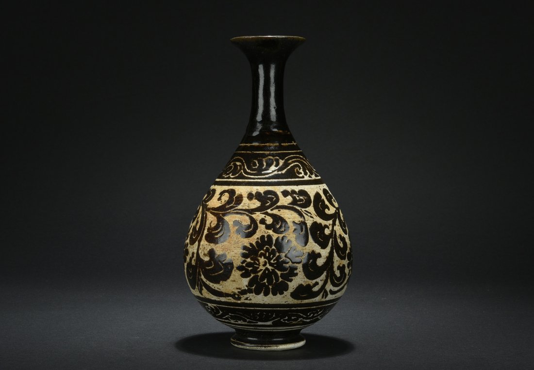 JIZHOU WARE FLOWER VASE: Of pear form with slender neck and flared rim, the vase's body depicts flowers and vines below ocean wave patterns, against black ground. Song Dynasty period. H: 11 5/8 in (29.5 cm) W: 6 in (25.2 cm)