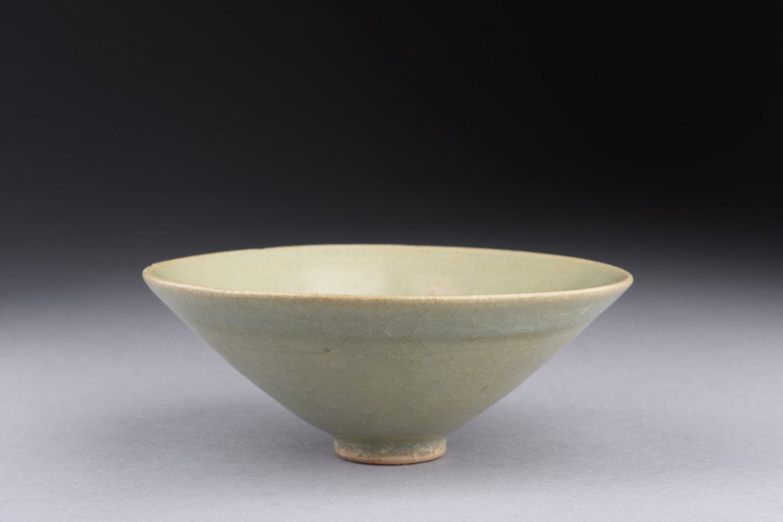 LONGQUAN WARE CONICAL BOWL: The conical shaped bowl glazed in celadon with crackle patterns, some kiln imperfections shown on the bowl, and the bottom unglazed. Ming Dynasty period or later. H: 2 in (5.1 cm) D: 5 1/8 in (13 cm)