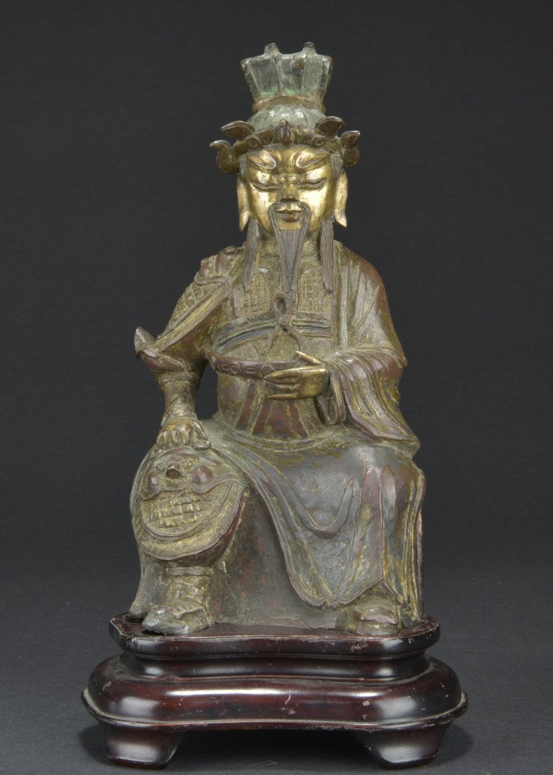 GILT BRONZE SEATED WARRIOR FIGURE: The warrior seated on the wooden stand, wearing full armor with beast mask patterns and partial robe, the downcast eyes and calm expression, with one hand on his knee and the other holding his belt. I