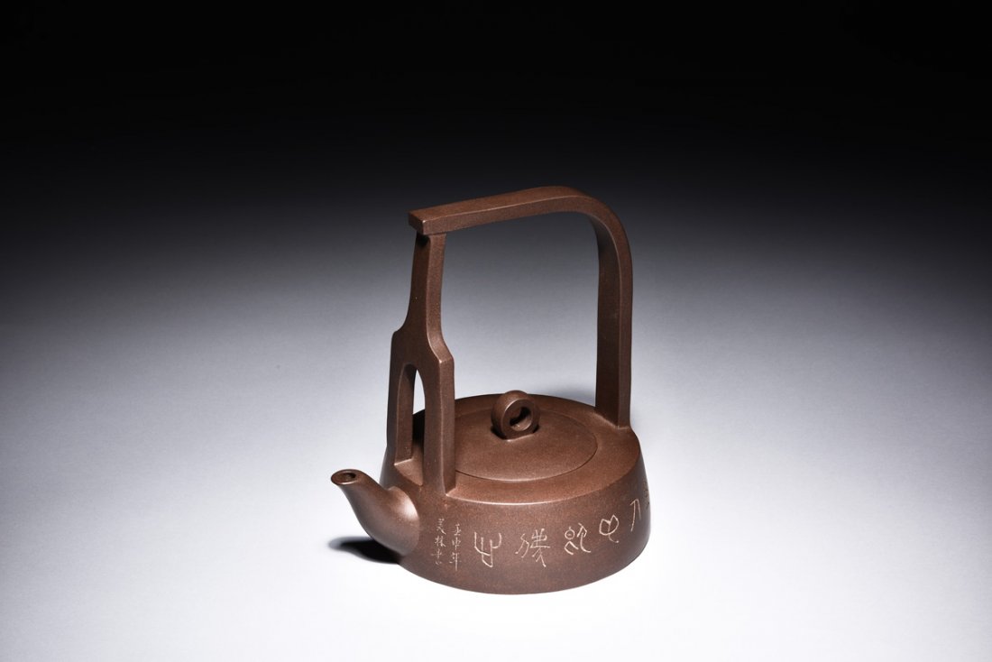 YIXING ZISHA STONEWARE TEAPOT: The teapot has a compressed body, side incised with calligraphy and signature, the tall raised handle attached to front and back, with elegant spout in front, mark on bottom.