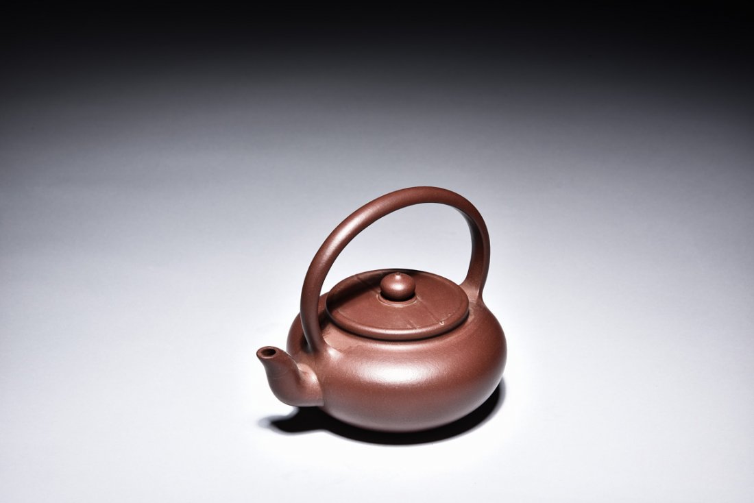 YIXING ZISHA STONEWARE TEAPOT: Of compressed form, the teapot's spout rises from brown body to rim level, the curved lifting handle arches above the flattened lid and bead finial, artist signature and mark beneath the lid and on th