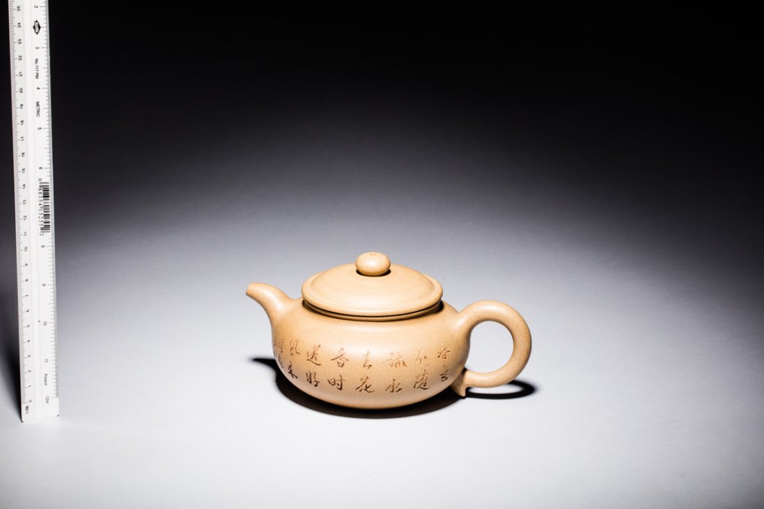 YIXING ZISHA 'POETRY' TEAPOT: Of compressed form, the teapot incised with poetry calligraphy on one side, bamboo trees and leaves on the reverse, body in light brown color, and bottom bears seven character mark.