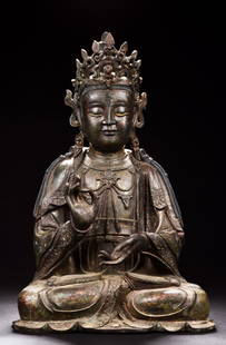 BRONZE CAST SEATED AVALOKITESHVARA FIGURE: Seated in dhyanasana, the Avalokiteshvara has one hand palm up, other hand raised in mudra, wearing elaborate and decorated robe, eyes closed in serene expression. Ming Dynasty period. Height: 23 in (