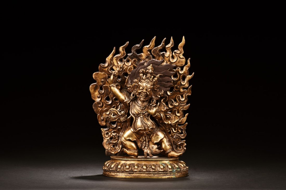 GILT BRONZE DHARMAPALAS FIGURE: Standing on top of lotus throne pad, wearing elaborate and intricate patterned robe with ornate crown, the Dharmapalas has wide open eyes, stretched arms, and curled legs, in front of flaming mandorla