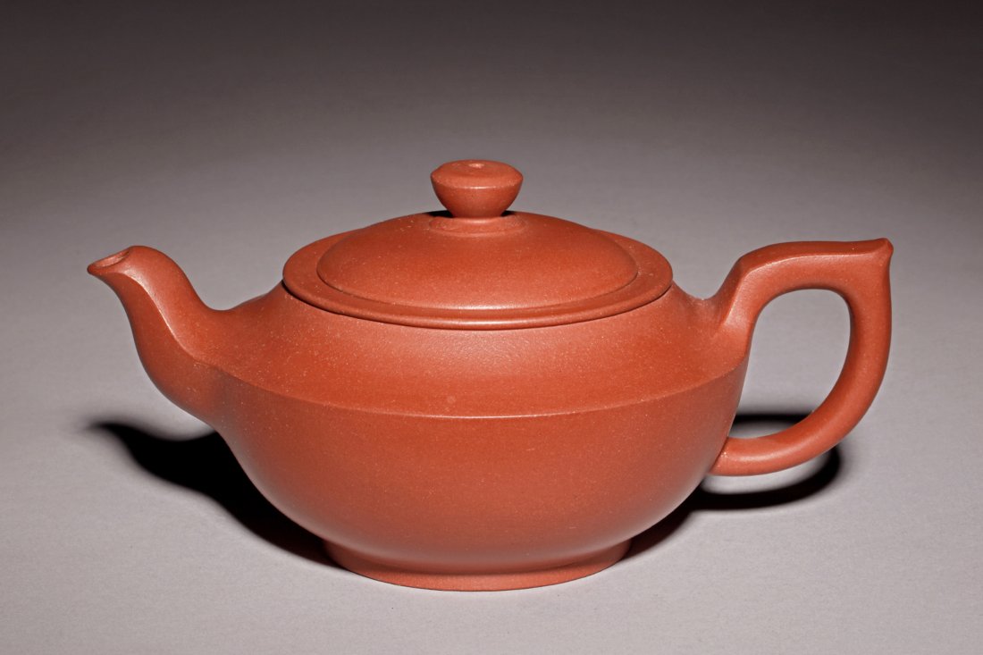YIXING ZISHA TEAPOT: The Yixing Zisha stoneware teapot is of creased edge tapering sharply from shoulder form, the longest dimension measuring Width: 7 in (17.8 cm), the clay is of reddish brown color tone, and the teapot