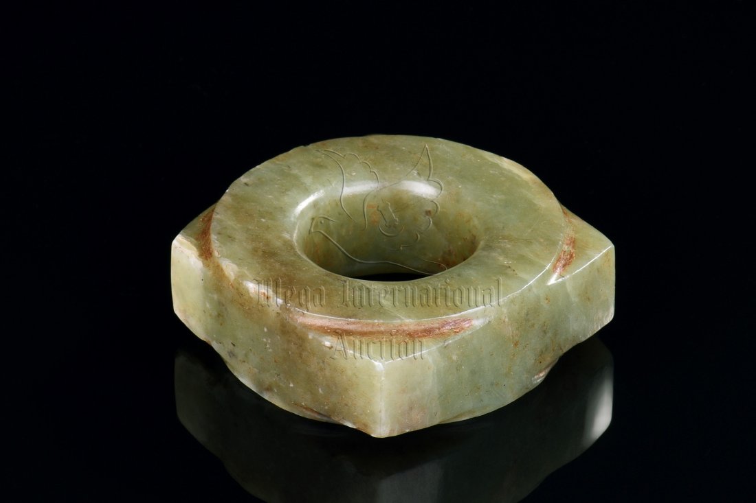 A PALE GREYISH-GREEN JADE CONG: With flat sides and a shallow collar at each end, the semi-translucent, pale greyish-green stone now has areas of brown and buff opaque alteration. Length: 2 1/4 in (5.7 cm) Width: 2 1/4 in (5.7 cm) W