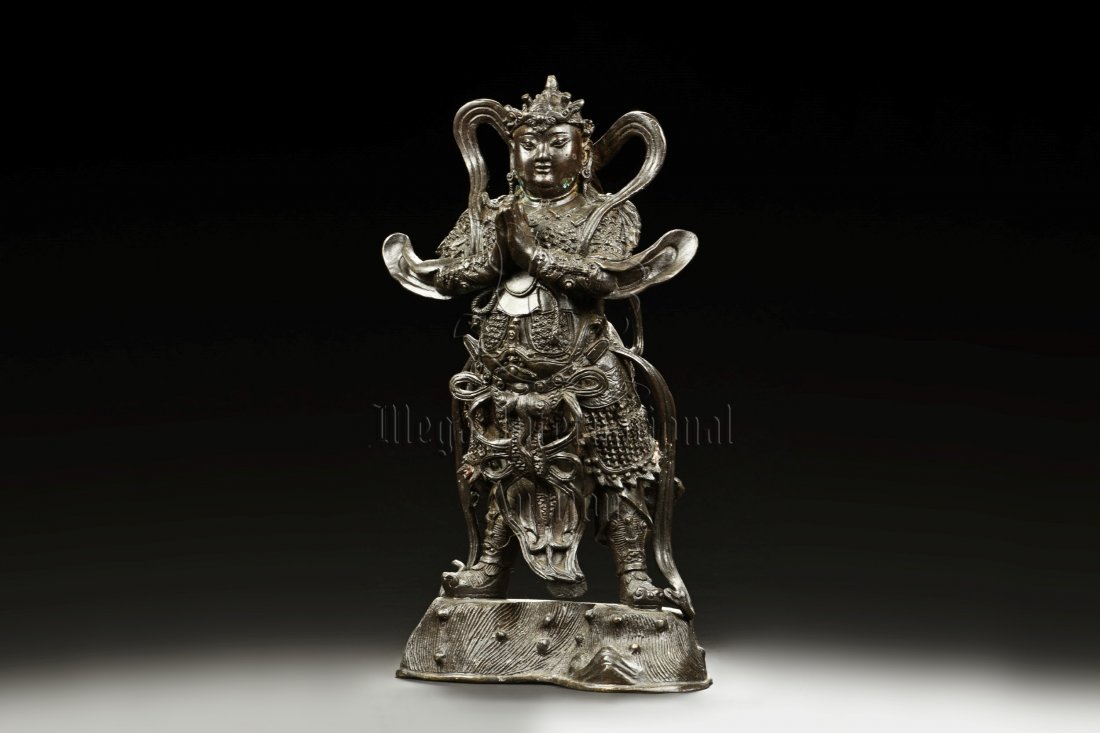 CAST BRONZE GUARDIAN SKANDA FIGURE: The cast bronze Guardian Skanda figure is heavily cast with stern expression, mounted standing on bronze stand and modelled wearing elaborate chain-mail armor with legs slightly apart and celestial ri