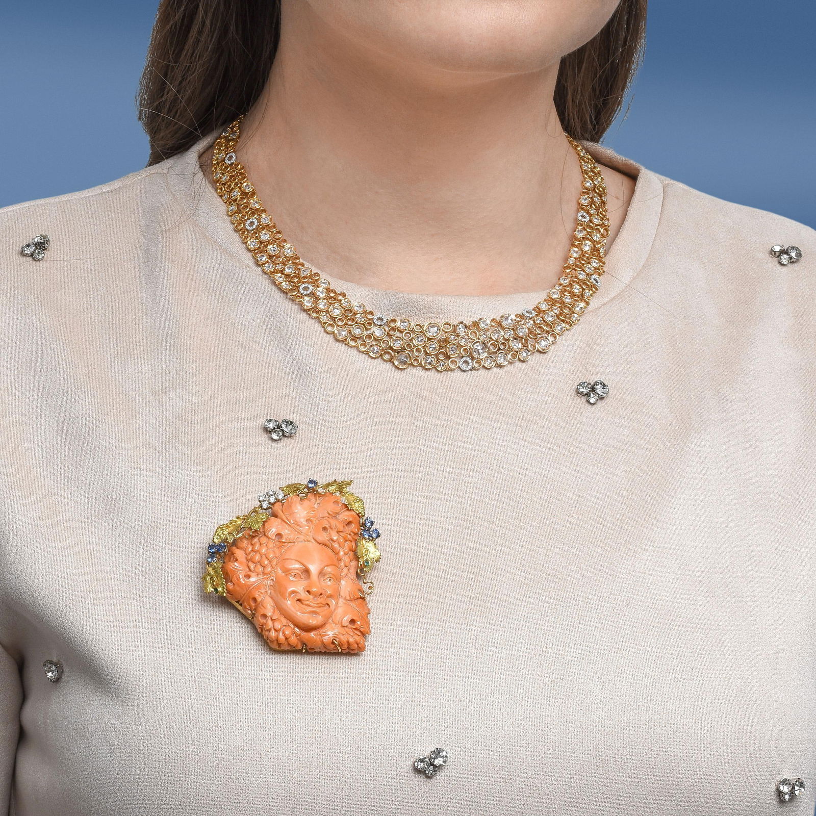 Vintage Bacchus in Grapevines Carved Coral Brooch: Summary of Key Characteristics • Metal: 18K yellow gold • Gemstone(s): Round brilliant cut diamonds approx.0.20 carats total; sapphire accents • Measurements: 2 1/2 inches long 