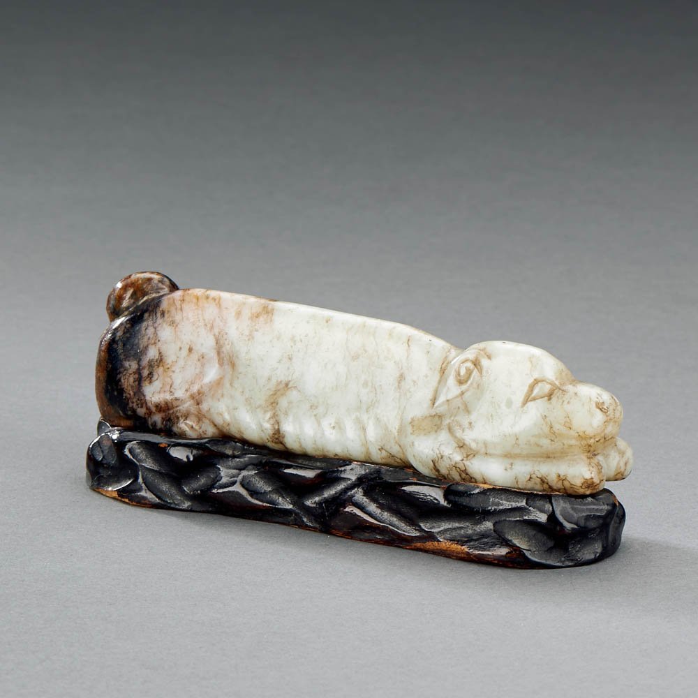 A CHINESE PALE CELADON AND RUSSET JADE RECUMBENT DOG: MING DYNASTY (1368-1644) A CHINESE PALE CELADON AND RUSSET JADE RECUMBENT DOG 明 青白玉帶沁「臥犬」 L 11 cm (4 3/8 in.)