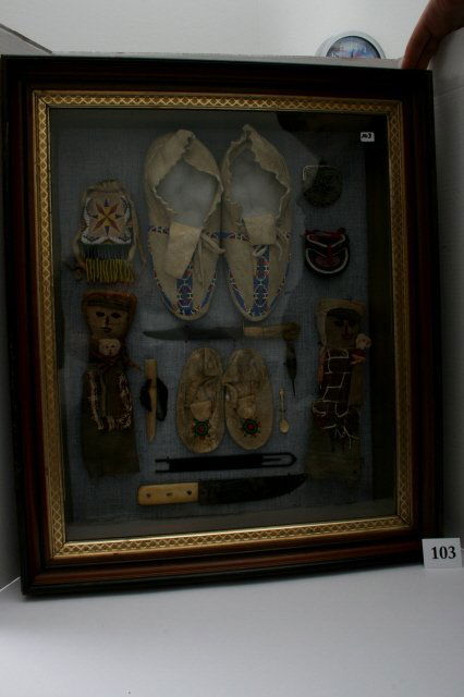 Plains Indian Items: 26" x 22" Antique Wood Frame Display of Plains Indian Items: Woman's & Childs Moccasins, small beaded pouch, two bone handled 19th century knives, iron weaving shuttle, small bone spoon, awl & husking
