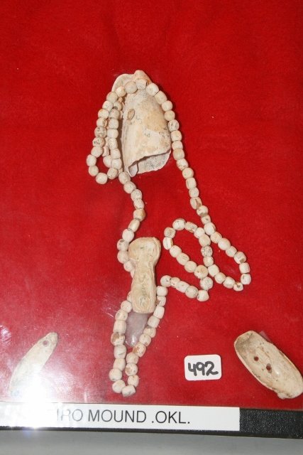 Shell Necklace, Miniature Shell Pendant: 8 x 12” Frame containing Shell Necklace, Miniature Shell Pendant, Gorget, Plug, Large Pendant, Spiro Mound – Oklahoma – Ex. May Guard Coll.