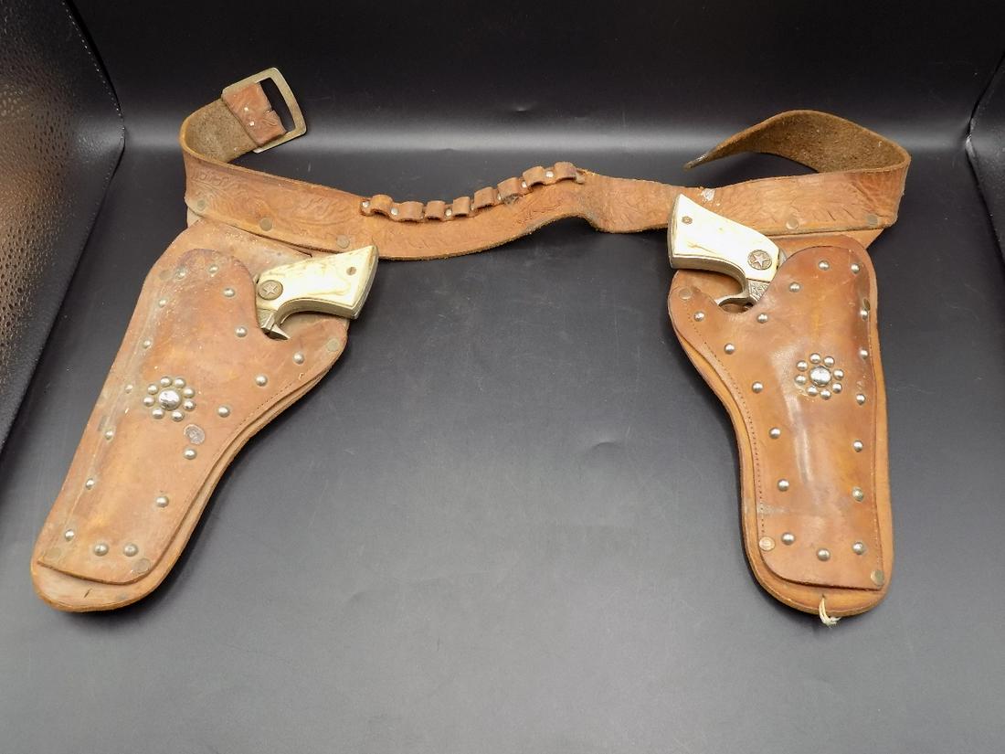 Vintage child’s western cowboy double holster cap guns: Vintage child’s western cowboy double holster cap guns. Texan Jr. marked on cap guns. Long horn steer on handles and elaborately decorated. Need clean and washed up. Leather belt measures approx. 31