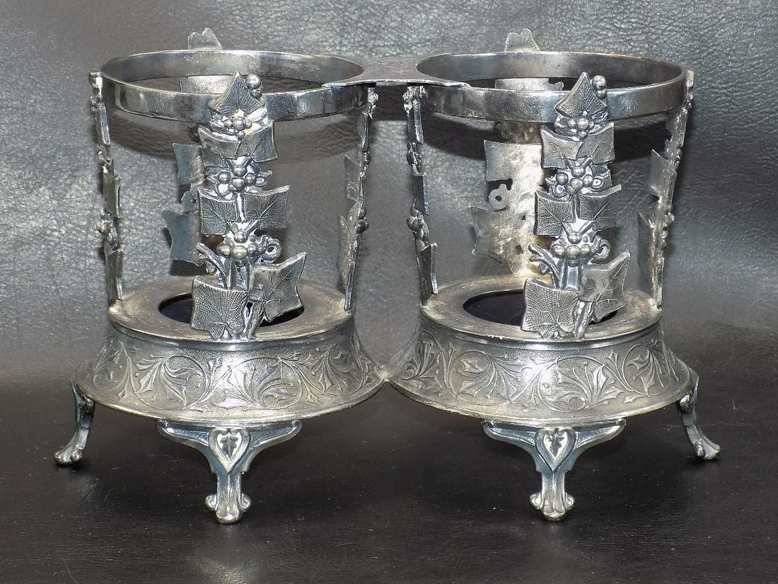 Ornate vintage double silverplate wine holder: Ornate vintage double silverplate wine holder. Grapevines surrounding sides. Did not find a maker marking. Great quality and detail. 5 ½ inches tall. 9 inches wide at feet. Opening for bottle 3 &