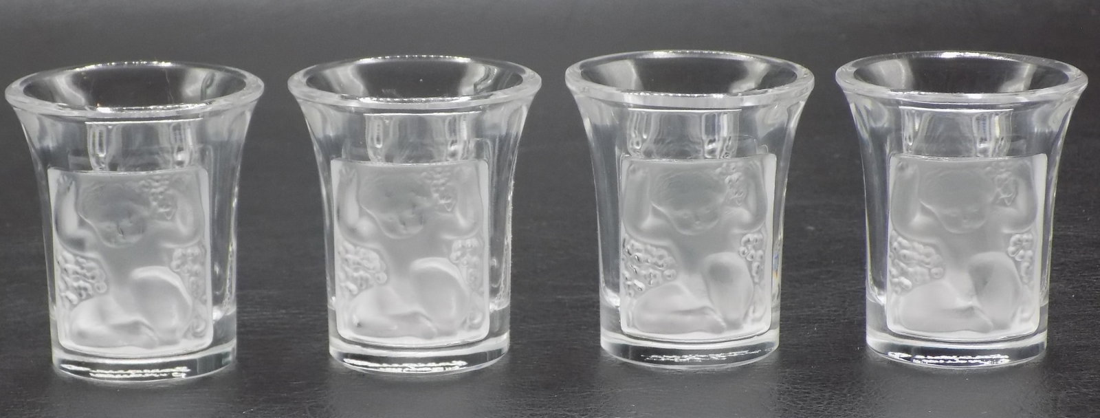 Four vintage signed Lalique art glass shot glasses with cupid: Four vintage signed Lalique art glass shot glasses with cupid. Signed on bottom as shown in photos. Cupids on two sides. In very good original as found condition. 1 7/8 inches tall