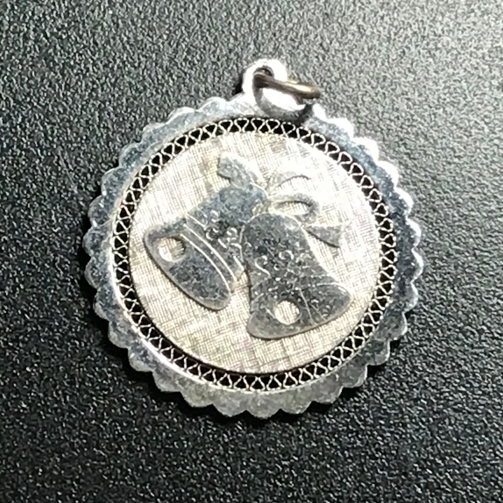 round silver pendant. 2 bells decorate front: round silver pendant. 2 bells decorate front