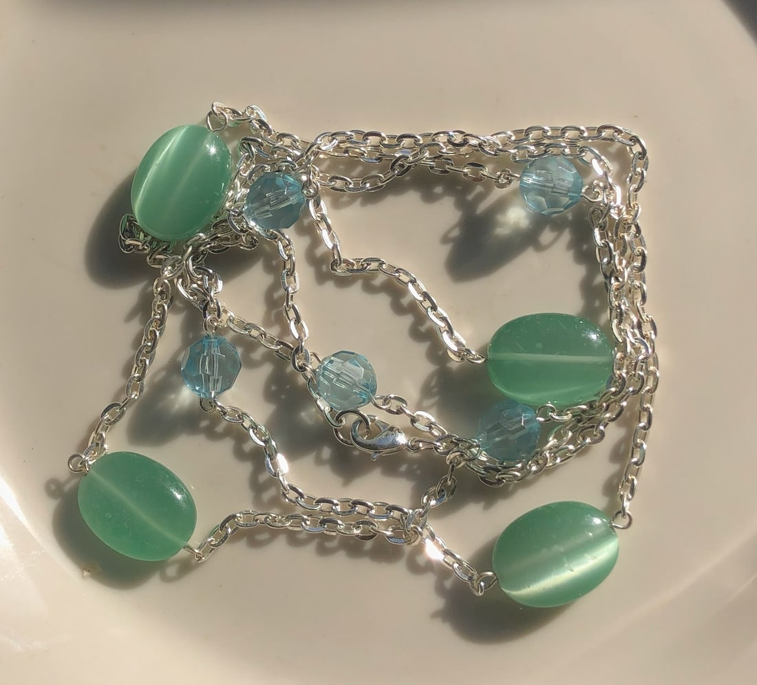 Green and Blue Beaded Necklace: A stylish necklace featuring green and blue beads on a silver chain.