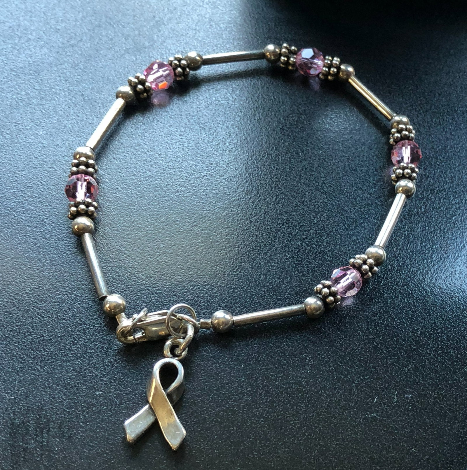 Pink Ribbon Silver Bracelet: A stylish silver bracelet featuring pink beads and a ribbon charm, symbolizing support and awareness.