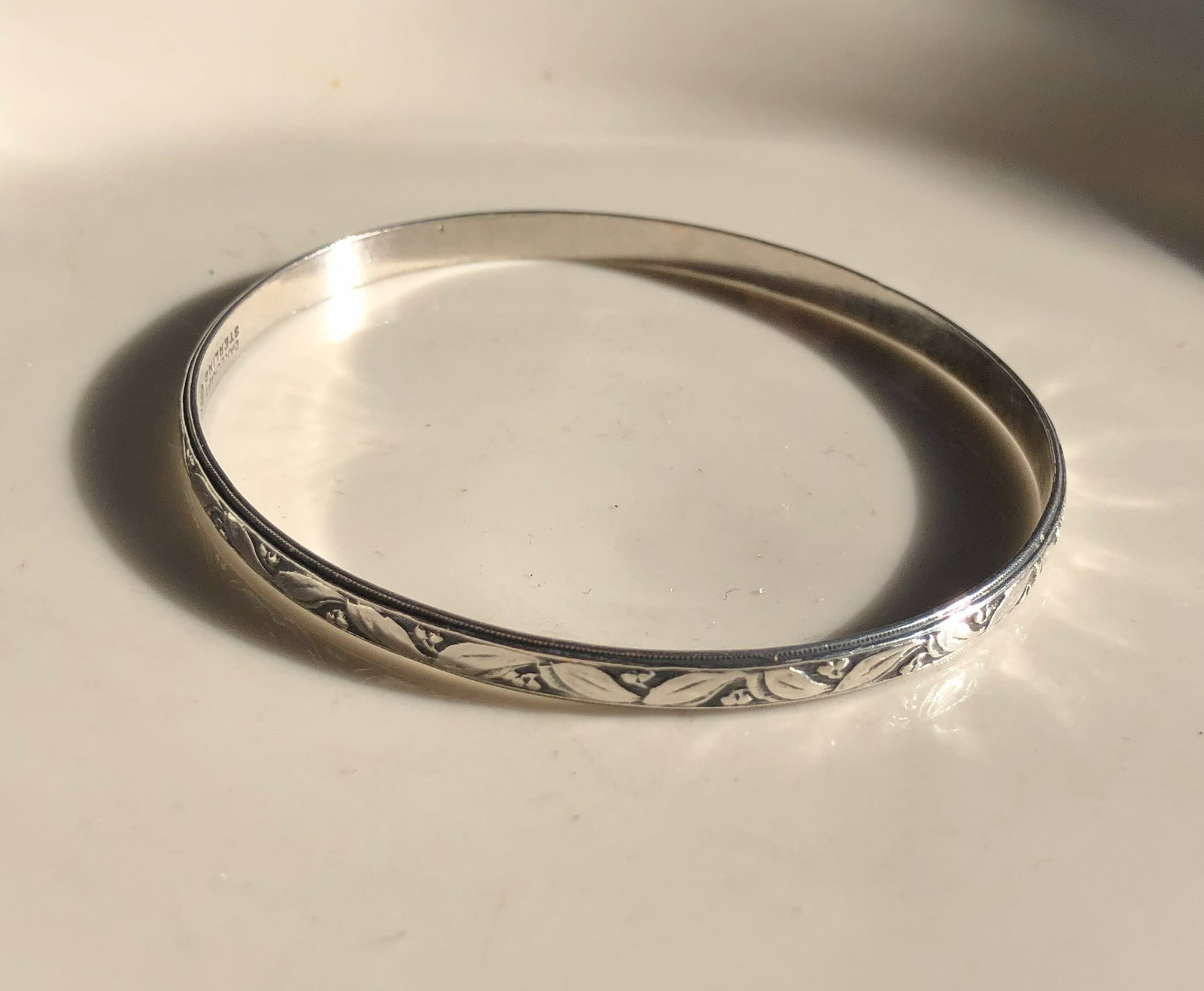 Silver Bangle Bracelet: Elegant silver bangle bracelet with intricate leaf pattern design.
