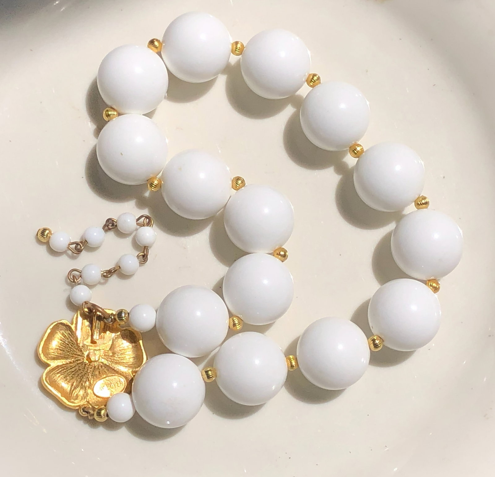 Elegant white bead necklace featuring gold accents and a gold floral charm.: Elegant white bead necklace featuring gold accents and a gold floral charm.