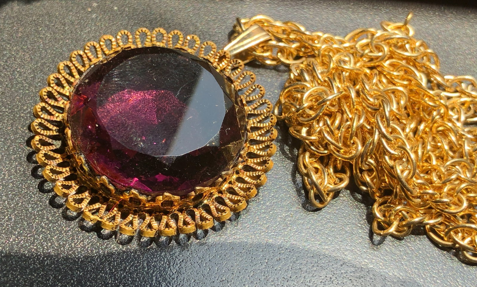 A stunning vintage gold color pendant necklace featuring a large purple gemstone. Perfect for