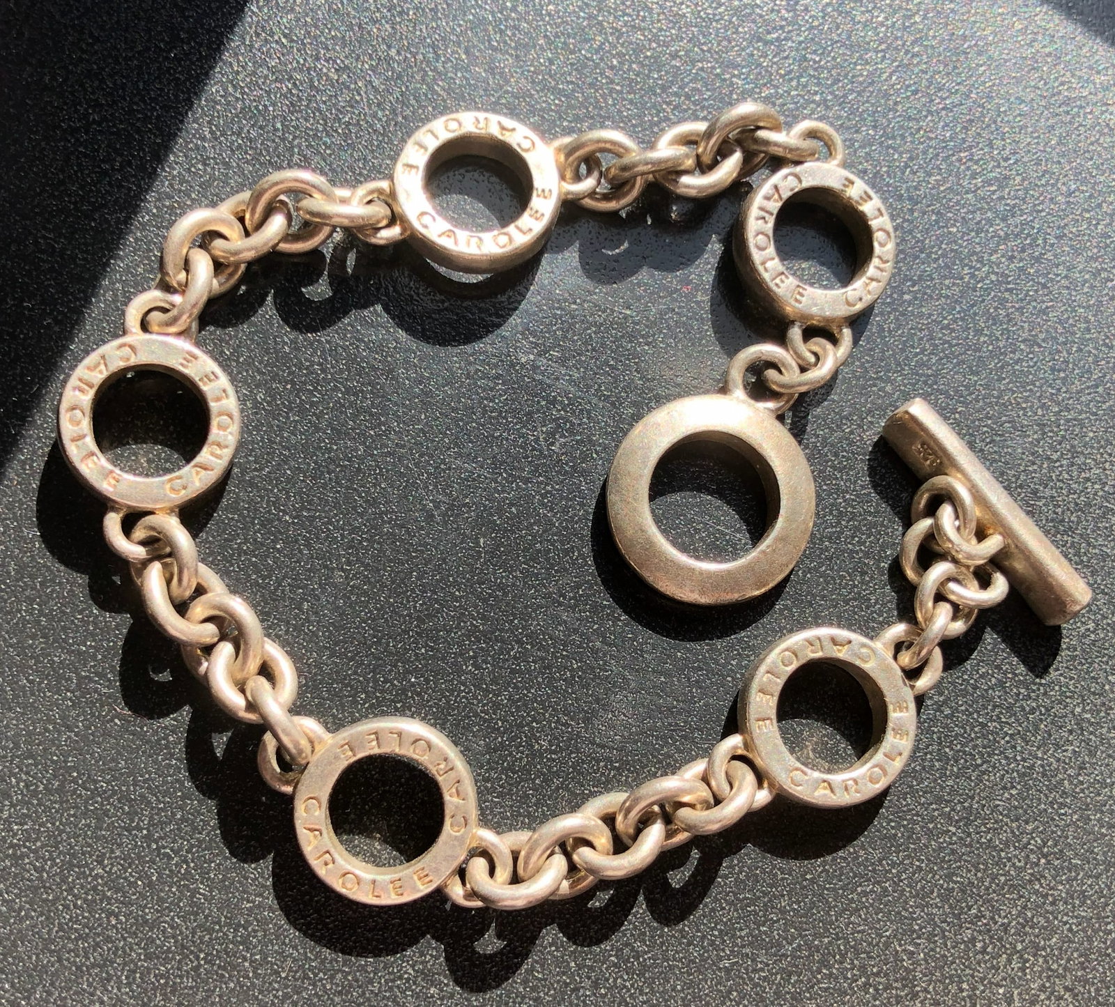 Carolee Silver Open-Link Toggle Bracelet: Silver Carolee bracelet composed of five signed open circular links joined by chain links and completed with a toggle clasp, showing surface wear and patina consistent with prior use.