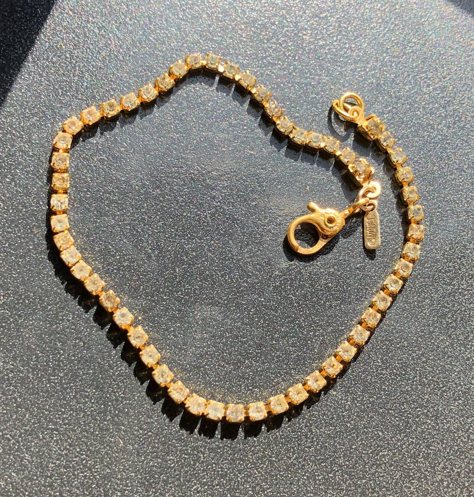 Gold-Tone Rhinestone Tennis Bracelet: Gold-tone line bracelet set with a continuous row of round clear rhinestones and finished with a lobster-claw clasp, showing light wear from previous use.
