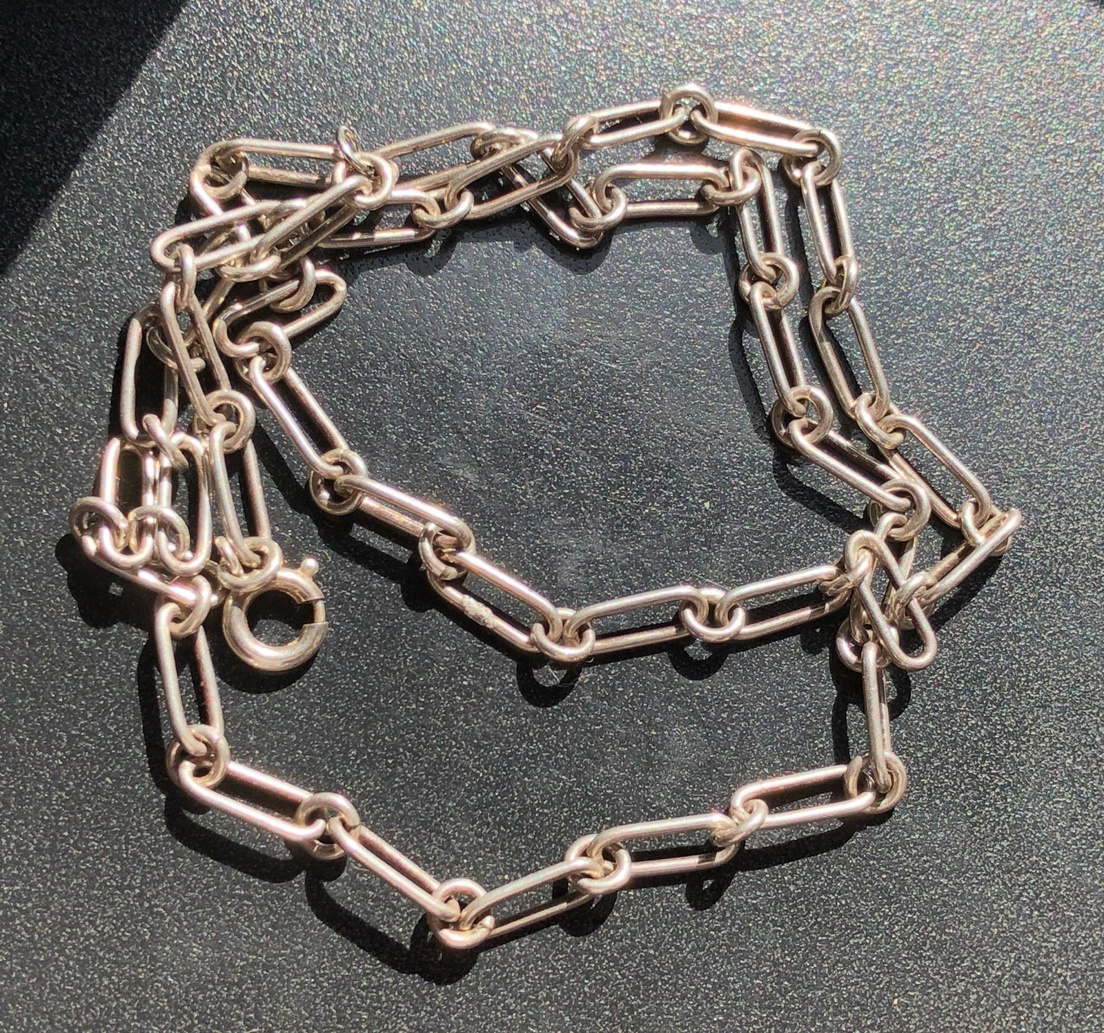 Silver Paperclip-Link Chain Necklace: Long silver chain composed of elongated paperclip-style links and fitted with a spring-ring clasp, showing surface wear and patina consistent with use.