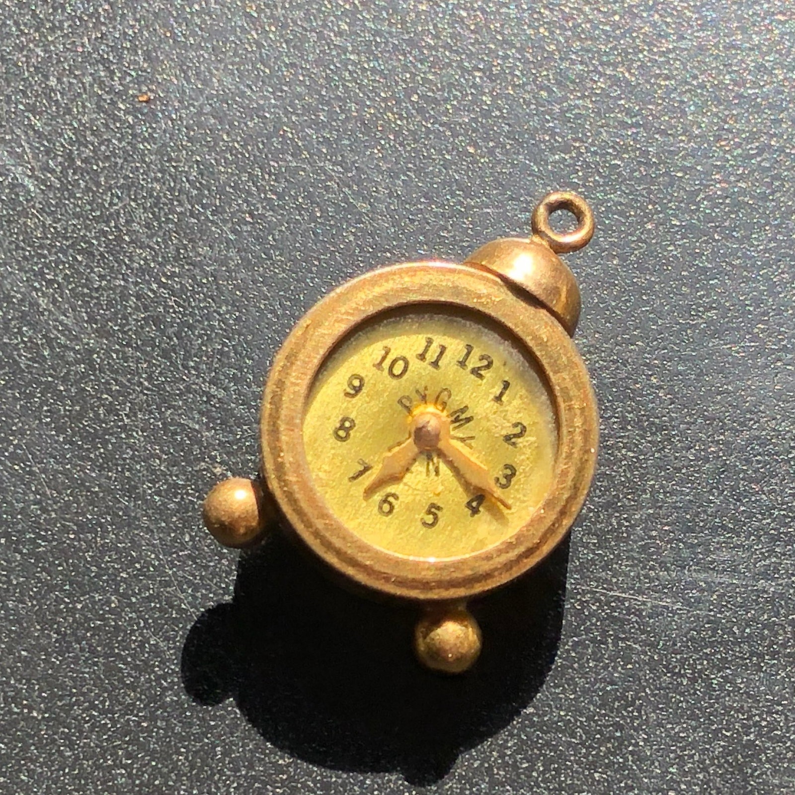 Miniature Alarm Clock Charm: Novelty gold-tone miniature alarm-clock charm with an Arabic-numeral dial, two bell-form feet, and a suspension loop, with timekeeping function untested.