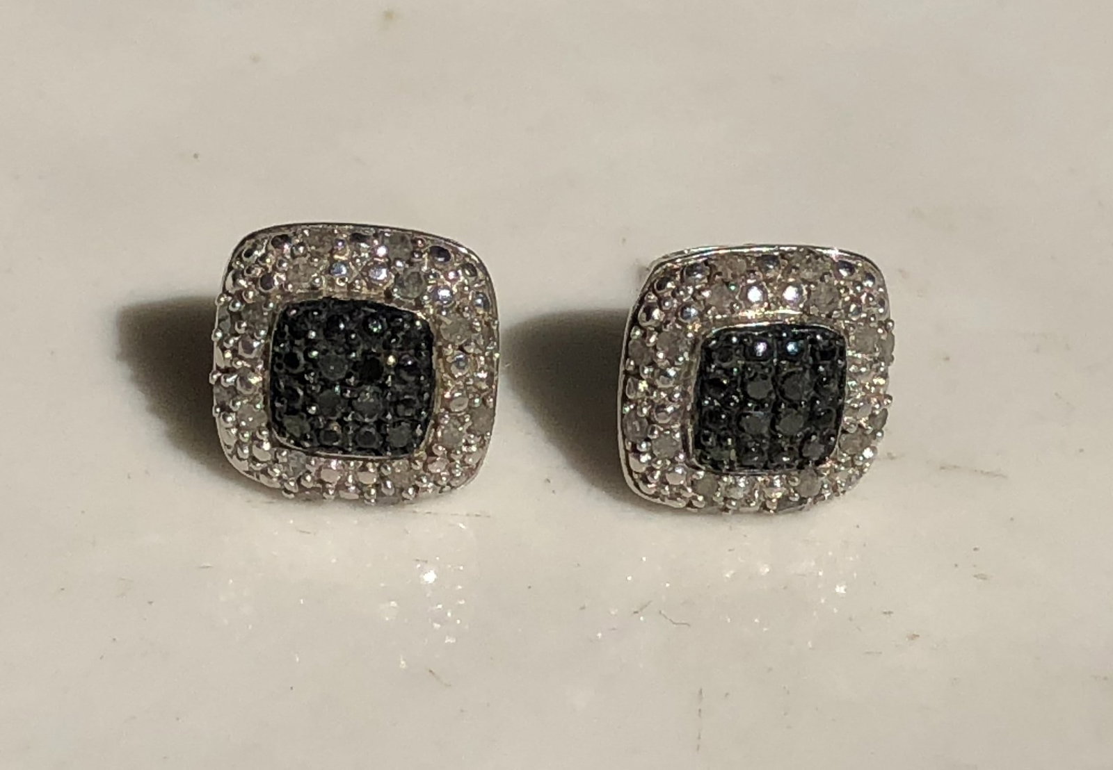 Square Pav?-Style Silver Stud Earrings: Pair of square pierced Silver stud earrings with dark central stone clusters surrounded by clear pav?-style accents, with stones and metal content untested.