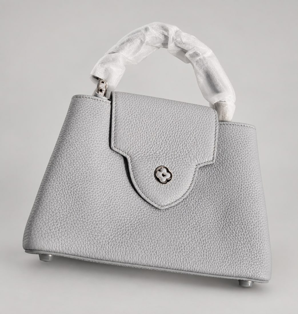 New Light Gray Pebbled Top-Handle Handbag: A structured light-gray pebbled top-handle handbag with a flap front, floral turn-lock closure, protective handle wrapping, and four rounded base feet, offered in new condition; Size: 10" x 11"