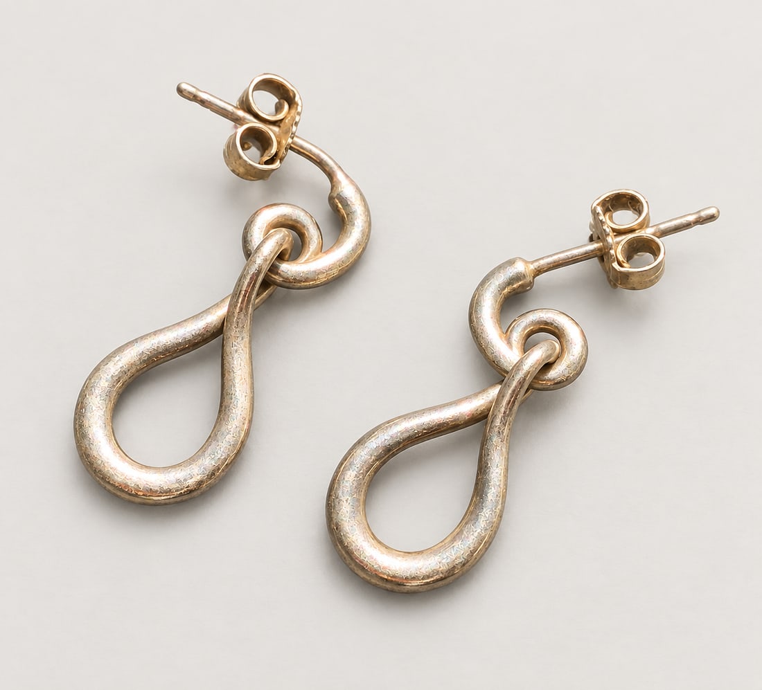 Pair of Infinity-Loop Drop Silver Earrings: A pair of Silver drop earrings formed as elongated infinity loops suspended from circular links and fitted with post-and-clutch backs, showing age-related surface wear
