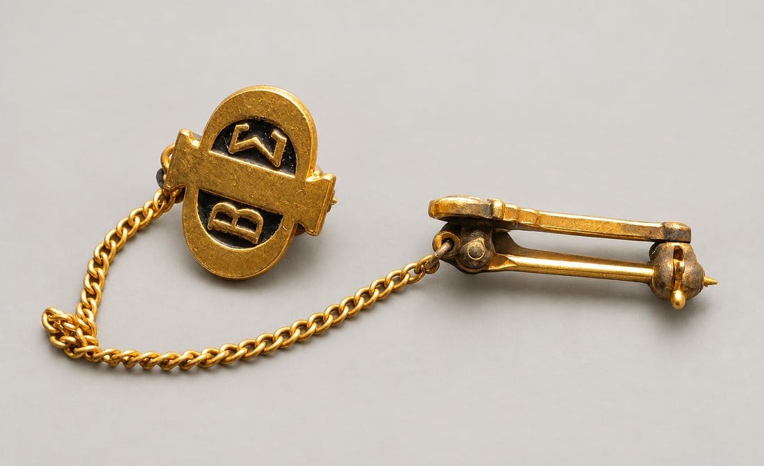 Gold-Tone Initial Safety Chain Brooch: A gold-tone safety-chain brooch or collar pin comprising an enamel initial medallion linked by a curb chain to a bar pin