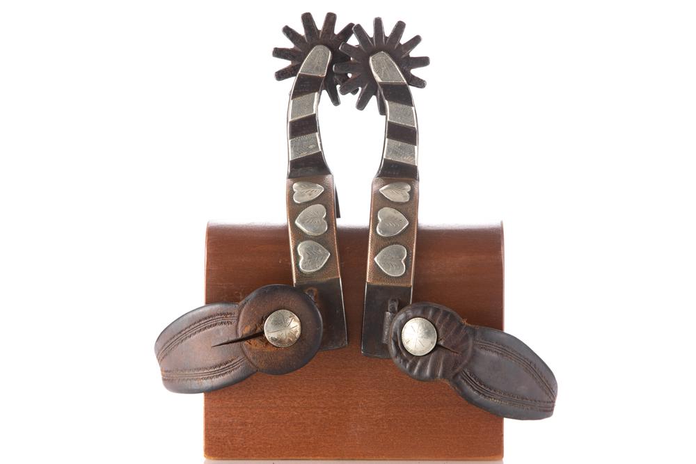 Pair of McChesney inside marked single mounted Spurs with engraved silver hearts overlayed on heel: Pair of McChesney inside marked single mounted Spurs with engraved silver hearts overlayed on heel bands. Spurs are mounted with a pair of vintage two-piece leather straps. Nice pair showing good cond