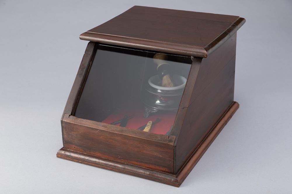 Small lift top wooden Display Case, table top model, measures 11" W x 15" L x 9 1/2" T. A: Small lift top wooden Display Case, table top model, measures 11" W x 15" L x 9 1/2" T. A silverplate and glass shaving mug with brush (some silverplate is missing) and three vintage straight Razors,