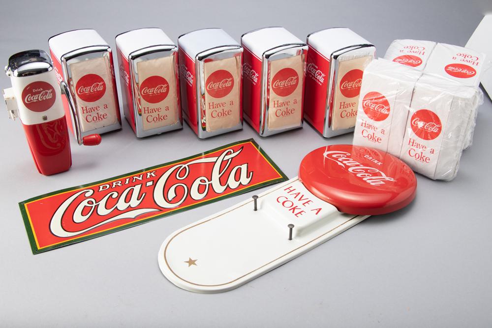 This lot consists of the following Coca-Cola Items: 5 Coca-Cola marked metal Napkin Dispensers; 4: This lot consists of the following Coca-Cola Items: 5 Coca-Cola marked metal Napkin Dispensers; 4 Packages of Napkin Refills; Metal and plastic Ice-o-Mat (ice crusher); 2 later Coca-Cola Advertising S