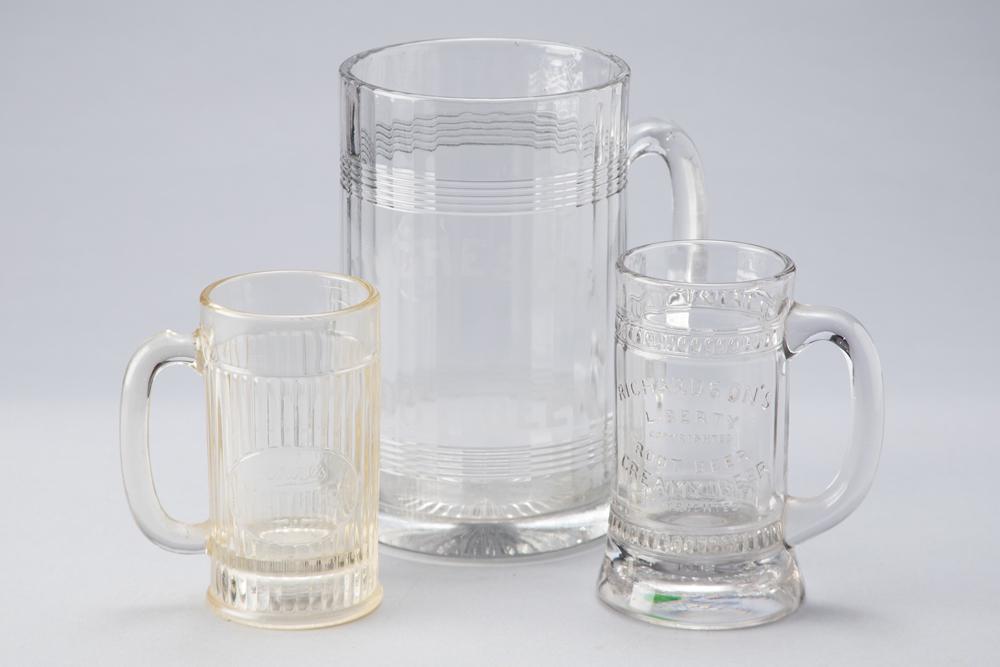 This lot consists of 3 vintage pressed glass Advertising Mugs: One for "Rochester Rootbeer",: This lot consists of 3 vintage pressed glass Advertising Mugs: One for "Rochester Rootbeer", measures 9 1/2" T x 6" diameter; One for "Richardson's Liberty Creamy Rootbeer", measures 6 3/4" T x 3 7/8"