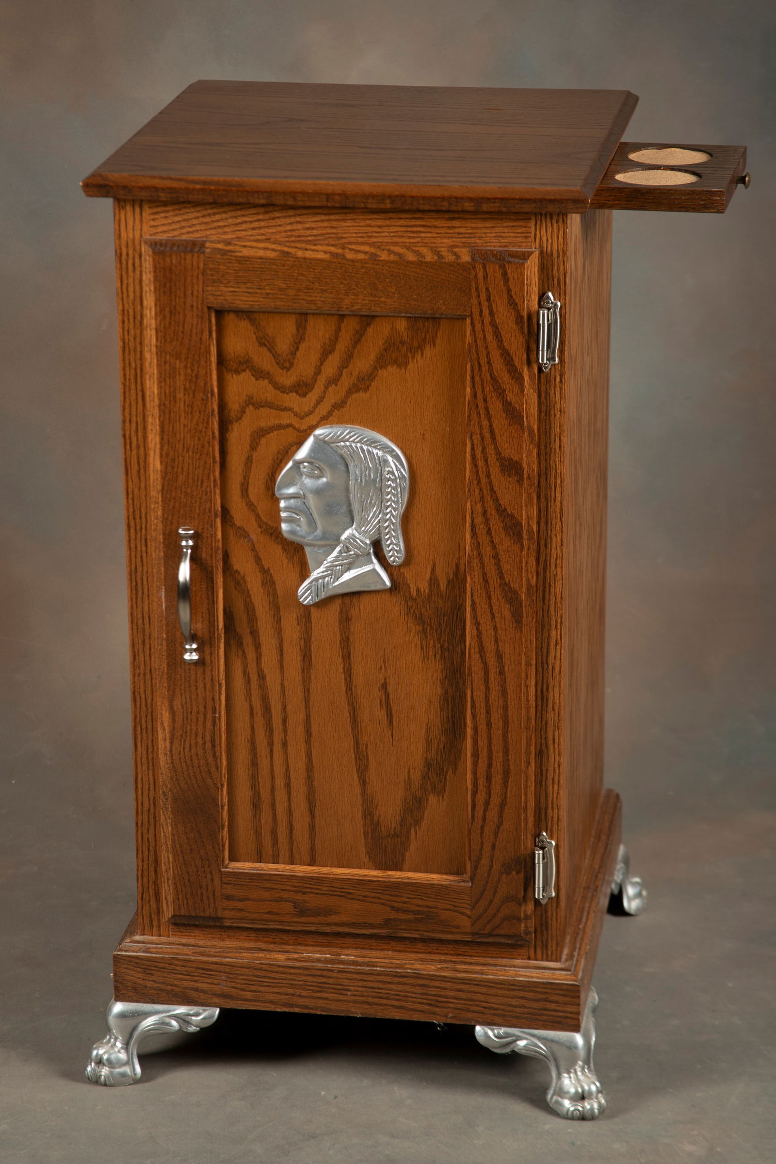 Oak Slot Machine Stand with single door, metal Indian Head on front and metal feet. Stand was custom: Oak Slot Machine Stand with single door, metal Indian Head on front and metal feet. Stand was custom made to fit most all table top slot machines. Measures 33 1/2" T x 17" Sq., nice finish and conditi