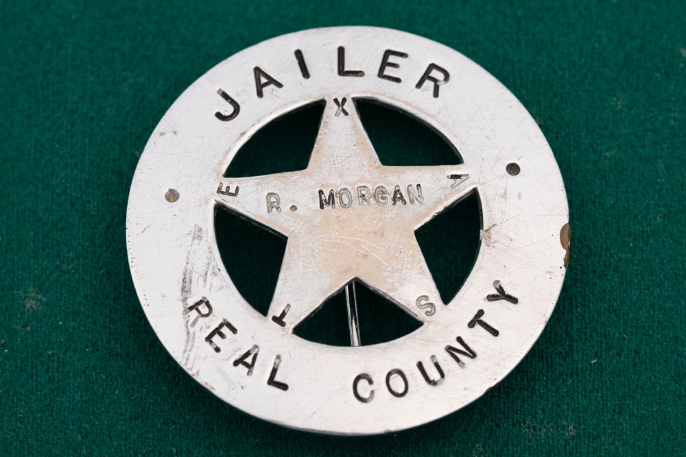 Circle 5-point cut-out Star Badge marked “JAILER/ REAL COUNTY?? with Star center marked “R.: Circle 5-point cut-out Star Badge marked “JAILER/ REAL COUNTY” with Star center marked “R. MORGAN” and “TEXAS’ spelled out on points. Measures 1 3/4” D with post pin and Burg